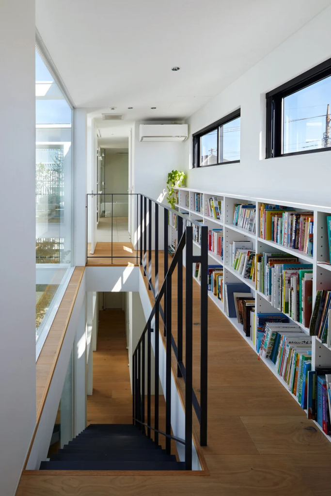 corredor que leva aos quartos conta com uma pequena estante metálica com livros, sem atrapalhar a passagem do projeto minimalista