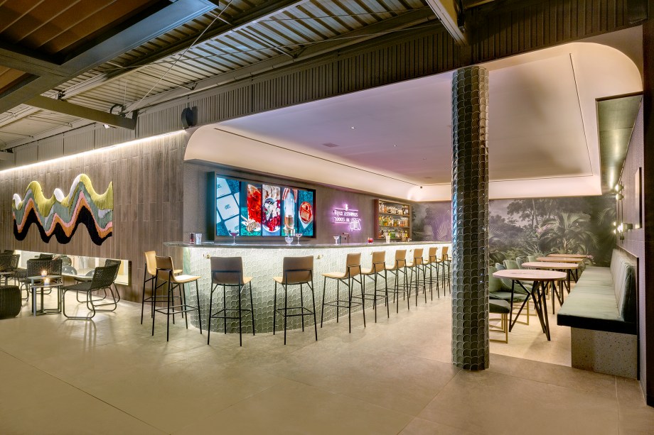 Studio Freijó - Altas Gastrobar. O espaço de 68 m² se inspira no estilo Neo Déco dos primeiros bares de coquetéis equilibrado com o tropicalismo do bar original do Altas. O projeto da arquiteta Natalie Tramontini e da designer de interiores Thalita Gonçalves, dupla à frente do Studio Freijó, tem rebuscamento nos materiais, como o veludo do banco, quartzito e porcelanato com acabamento metálico das paredes. Destaque para os acabamentos com diferentes texturas que compõem o ambiente. No local, obra de Carolina Kroff e um mural de Desireé Feldmann.