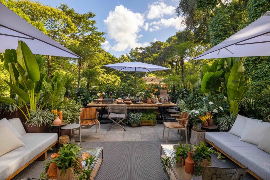 Anna Luiza Rothier - Muito Além do Jardim. Um recanto a céu aberto, ligeiramente protegido da chuva por ombrelones, e com espaço de sobra para encontros informais e descontraídos, que são a cara do Rio. Com vista para os jardins e para (quase) tudo o que acontece na área externa da casa, o terraço se insere ainda mais na paisagem natural do entorno com o uso de espécies diversas de plantas e a parede principal tomada por um jardim vertical. Um ambiente tropical, leve, despretensioso e bem carioca.