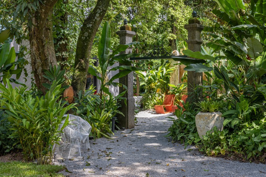 Catê Poli - Paisagismo Migrante. Um jardim tropical, com a exuberância da Mata Atlântica e a volta das bromélias. Localizado no entorno da Casa Migrante, num cantinho reservado dos vastos jardins da Residência Brando Barbosa, o espaço cria cenários atraentes que estimulam o convívio ao ar livre. Com muitas folhagens verdes e plantas nativas - que conversam perfeitamente com a arquitetura fluida da casa -, é um ambiente que convida o visitante a sentar, relaxar e curtir a natureza.