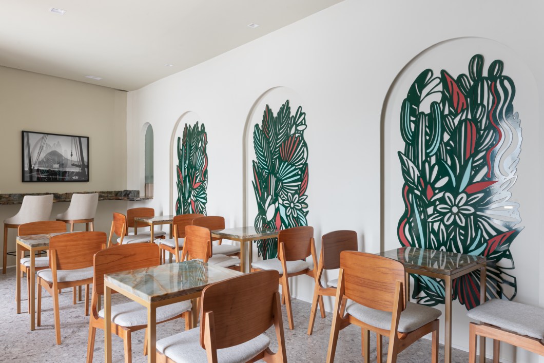 Renata Tristão - Café da Casa. Curvas, texturas, arte e cor: o café foge do usual e traz o conceito de "Cafeteria Galeria". Sem balcão ou qualquer produção visível, o ambiente se torna um espaço totalmente focado no bem-estar do usuário e brinca com os materiais e obras de arte expostas, convidando o visitante a aproveitar os 35 m² do salão, degustando de um bom café em um ambiente contemporâneo e autêntico. Os arcos iluminados abrigam uma arte exclusivamente pensada para o espaço, produzida pela artista Ana Paula Castro e inspirada no tema brasilidade. As mesas e balcão foram produzidos utilizando uma pedra fruto da primeira extração do bloco da rocha e mesclam tons de verde, dourado e azul. O espaço pretende ser palco para momentos de interação, arte, degustação e conquista com seu clima acolhedor e moderno. Renata Tristão - Café da Casa. Curvas, texturas, arte e cor: o café foge do usual e traz o conceito de "Cafeteria Galeria". Sem balcão ou qualquer produção visível, o ambiente se torna um espaço totalmente focado no bem-estar do usuário e brinca com os materiais e obras de arte expostas, convidando o visitante a aproveitar os 35 m² do salão, degustando de um bom café em um ambiente contemporâneo e autêntico. Os arcos iluminados abrigam uma arte exclusivamente pensada para o espaço, produzida pela artista Ana Paula Castro e inspirada no tema brasilidade. As mesas e balcão foram produzidos utilizando uma pedra fruto da primeira extração do bloco da rocha e mesclam tons de verde, dourado e azul. O espaço pretende ser palco para momentos de interação, arte, degustação e conquista com seu clima acolhedor e moderno.