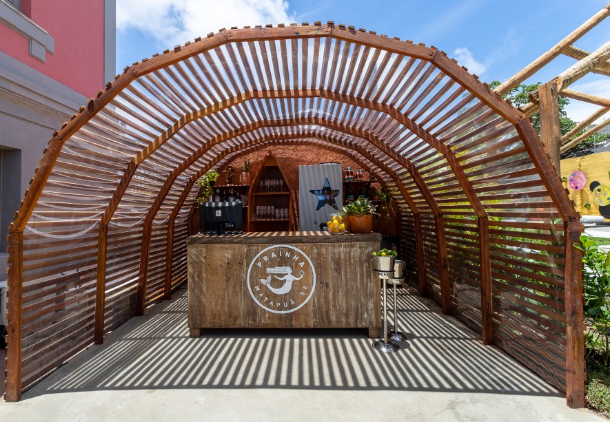 Barroso Melo e Augusta Ribeiro - Prainha Bar. Como um passeio à beira do rio, o projeto é um convite para contemplar a paisagem ao entardecer, respirando o ar fresco. O ambiente é envolto por madeira, pedras naturais, elementos manufaturados com simplicidade e rusticidade, ao mesmo tempo em que recebe acabamentos sofisticados e pontuados por cores quentes. Recursos luminotécnicos com cor vibrante e em estilo irreverente foram instalados para ressaltar o ambiente. O pórtico que recepciona os visitantes foi pensado para criar uma experiência sensorial para a mente e o corpo.