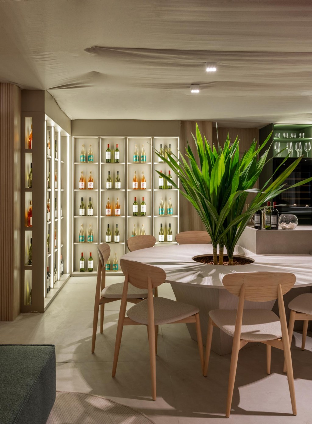 vilaville-arquitetura-restaurantes-horta-casacor-sao-paulo-2023-credito-favaro-jr (8) Vilaville Arquitetura - Restaurante Horta. Projeto da CASACOR São Paulo 2023. Na foto, mesa redonda com plantas, balcão de bar e adega iluminada.