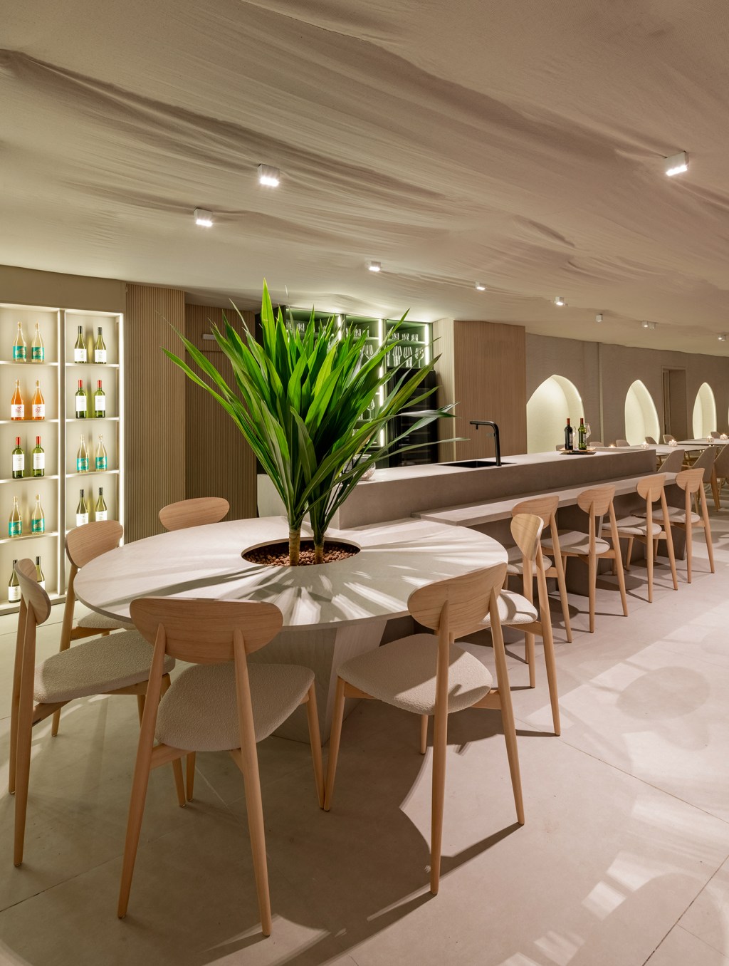 vilaville-arquitetura-restaurantes-horta-casacor-sao-paulo-2023-credito-favaro-jr (9) Vilaville Arquitetura - Restaurante Horta. Projeto da CASACOR São Paulo 2023. Na foto, mesa redonda com plantas, balcão de bar e adega iluminada.