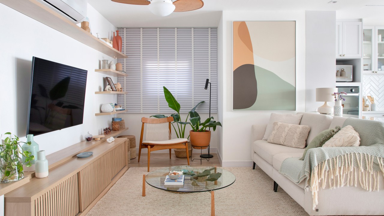 Duplex de 210 m² ganha décor na cor branca no estilo clássico e boho. Projeto de Amanda Miranda. Na foto, sala de estar com tv, quadro, sofá e tapete.