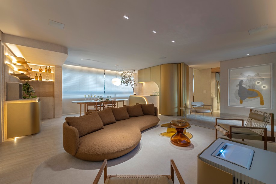 Renata Machado e André Magalhães Arquitetura e Design - Sala e lavabo do apartamento. A ideia de refúgio urbano em contraposição ao frenesi do dia a dia está traduzida principalmente na presença marcante das formas orgânicas e na escolha de uma paleta de cores suaves que transmite fluidez e serenidade. Um ambiente interativo que utiliza a tecnologia a favor da praticidade. Parte do revestimento é em travertino, trabalhado tanto na pedra lisa como ranhurada, presente no lavabo, com mesmo conceito orgânico, na adega e no bar.