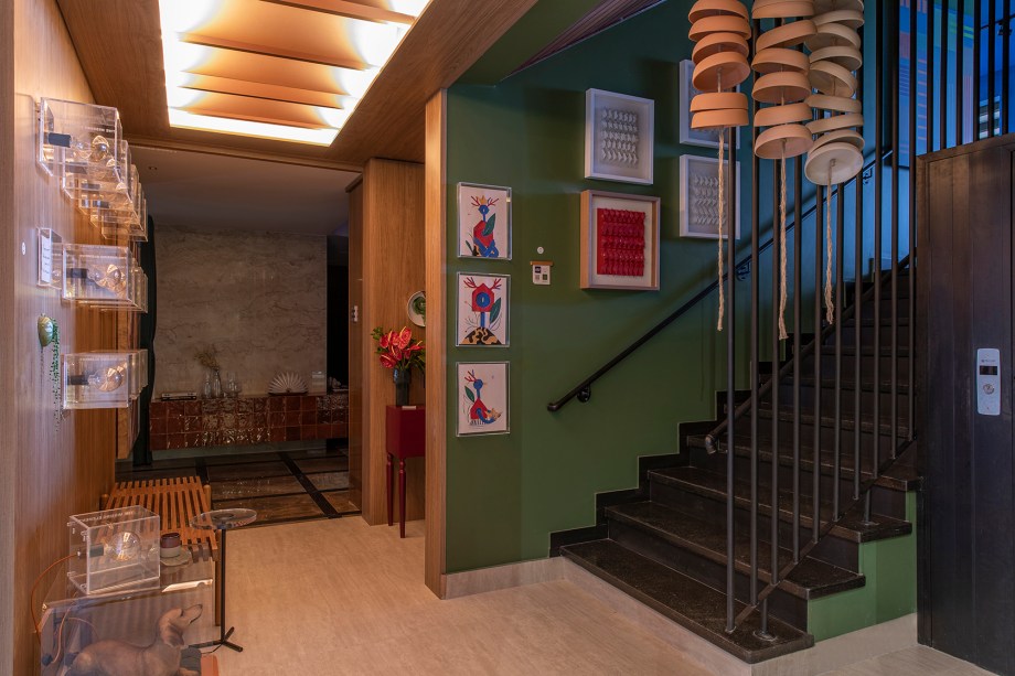 Bete Said e Rodi Albano - Hall Ojo. Não há como entrar na CASACOR sem ser impactado pelo OJO, espelho assinado por Bete Said. A peça chama a atenção pelo design e por sua tecnologia, com iluminação RGB, carregador de smartphones por indução e assistente de voz. É um convite para olhar ao redor, observar cada detalhe. Como a caixa de acrílico da Soul Artsy Brand com a foto de uma árvore (Eloá Fernandes), ponto de partida do projeto. “Representamos a busca pela saúde mental no mundo pós-pandêmico de várias formas. Essa árvore, que fica em um hospital psiquiátrico, remete aqui à prisão de nossa própria natureza através dos delírios da loucura”. Para as profissionais, as obras de arte (Inn Gallery), que formam uma verdadeira galeria, expressam a loucura de forma livre, através de manifestações autorais. “E o OJO nos faz questionar a inteligência artificial, quem está ‘olhando’ quem”. Não por acaso, a cor predominante é o verde, que proporciona tranquilidade, equilíbrio. “Nosso espaço convida a enxergar o belo, para não enlouquecer com a vida moderna”.