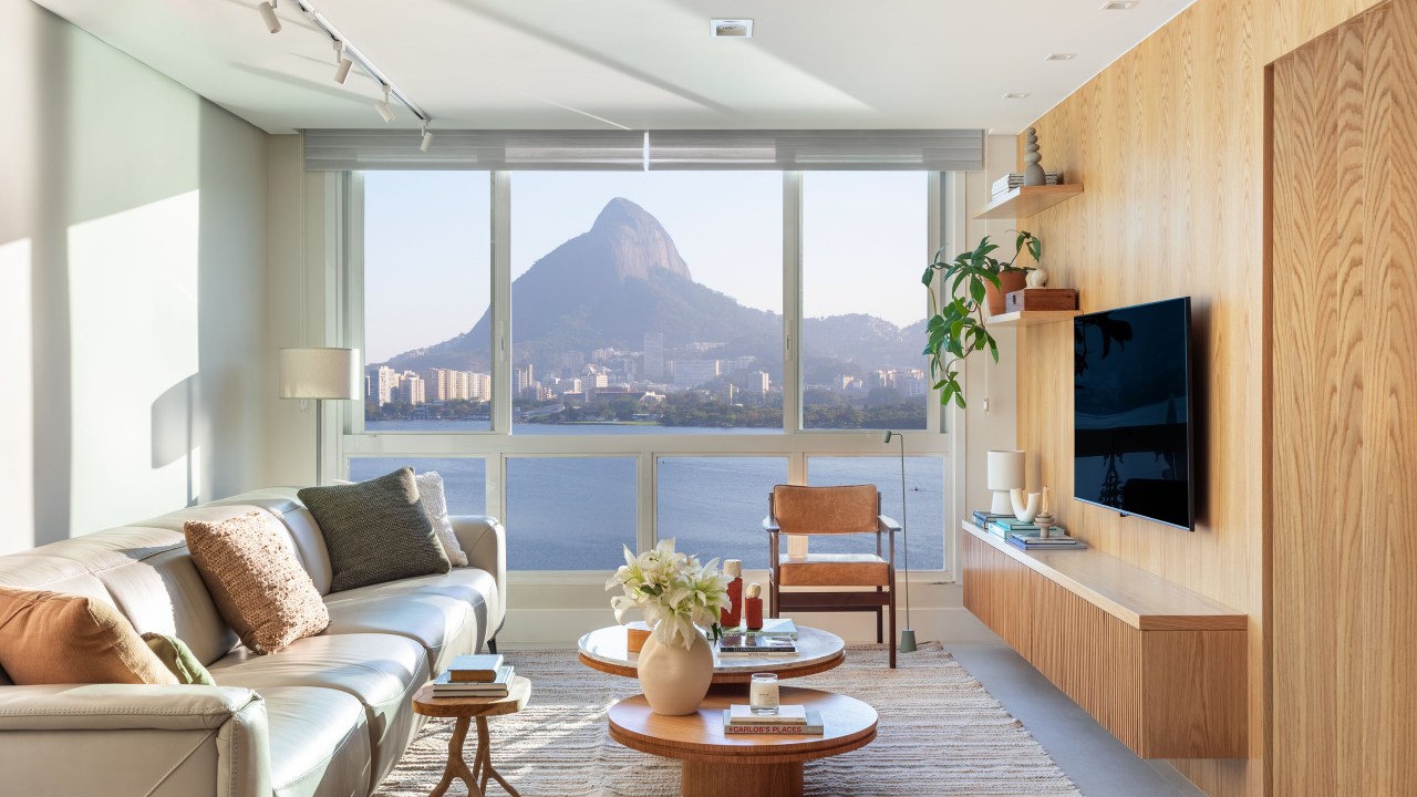 Apartamento de 190 m² tem vista para o Cristo Redentor de todos os cômodos. Projeto Beta Arquitetura. Na foto, sala de estar com tv, parede de madeira e vista para a lagoa.
