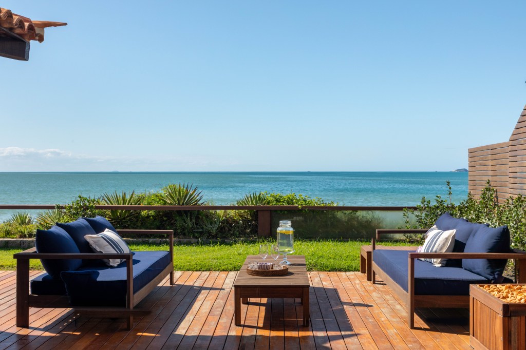 Venezianas azuis na varanda marcam esta casa de praia inspirada na Grécia. Projeto de Brise Arquitetura. Na foto, varanda com vista para o mar e deque de madeira.