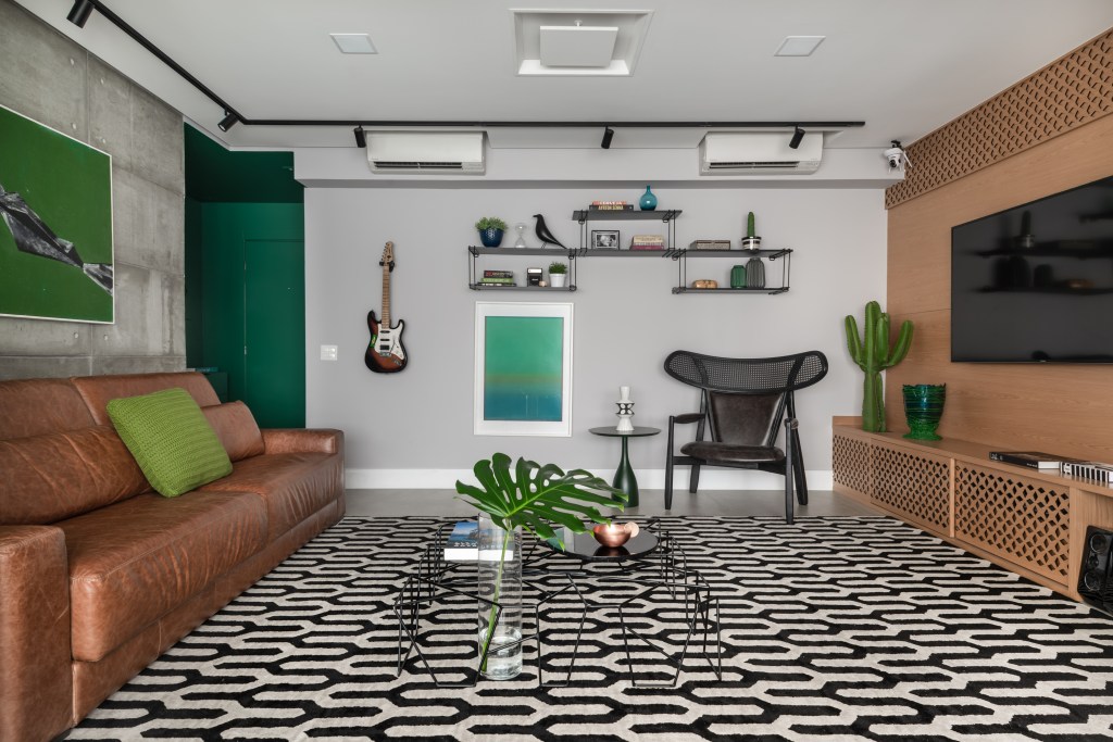 Beatriz Quinelato ARQ – AP Fernanda – Pinheiros @escanhuelaphot Painel retrátil esconde a churrasqueira neste apê descolado de 120 m². Projeto de Beatriz Quinelato. Na foto, sala de estar com parede verde, sofá de couro e tapete estampado.