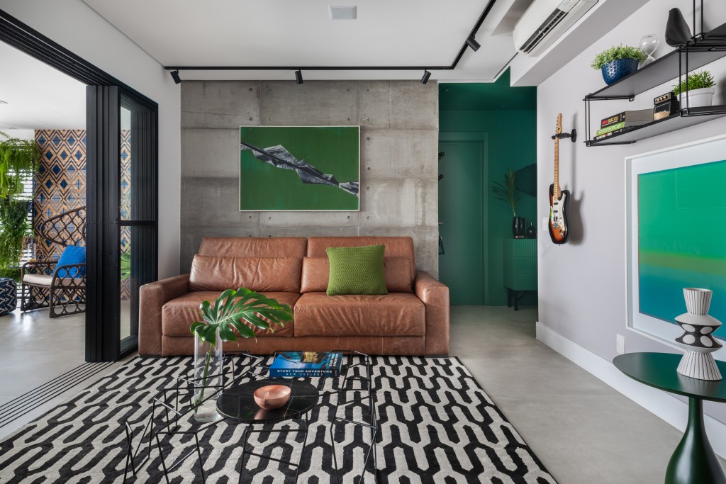 Beatriz Quinelato ARQ – AP Fernanda – Pinheiros @escanhuelaphot Painel retrátil esconde a churrasqueira neste apê descolado de 120 m². Projeto de Beatriz Quinelato. Na foto, sala de estar com parede verde, sofá de couro e tapete estampado.