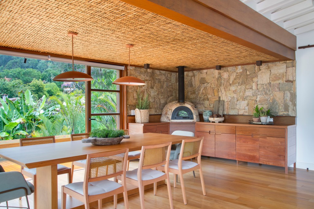 suite-casa-campo-bangalo-suspenso-meio-natureza-escala-arquitetura-credito-juliano-colodeti (20) Suíte de casa de campo fica em bangalô suspenso no meio da natureza. Projeto de Escala Arquitetura. Na foto, sala de jantar com teto de fibra e vista para o jardim. Churrasqueira e parede de pedra.