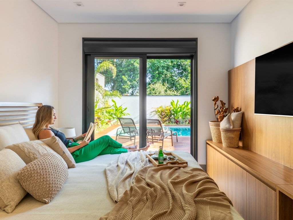 Pensada para veraneio, casa em meio ao verde vira o lar oficial da família. Projeto de Pietro Terlizzi. Na foto, quarto com tv e vista para o piscina.