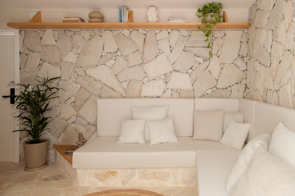Reforma transforma imóvel de 45 m² em refúgio tropical. Projeto de Tauari Arquitetura. Na foto, sala com parede de pedra e sofá de alvenaria.
