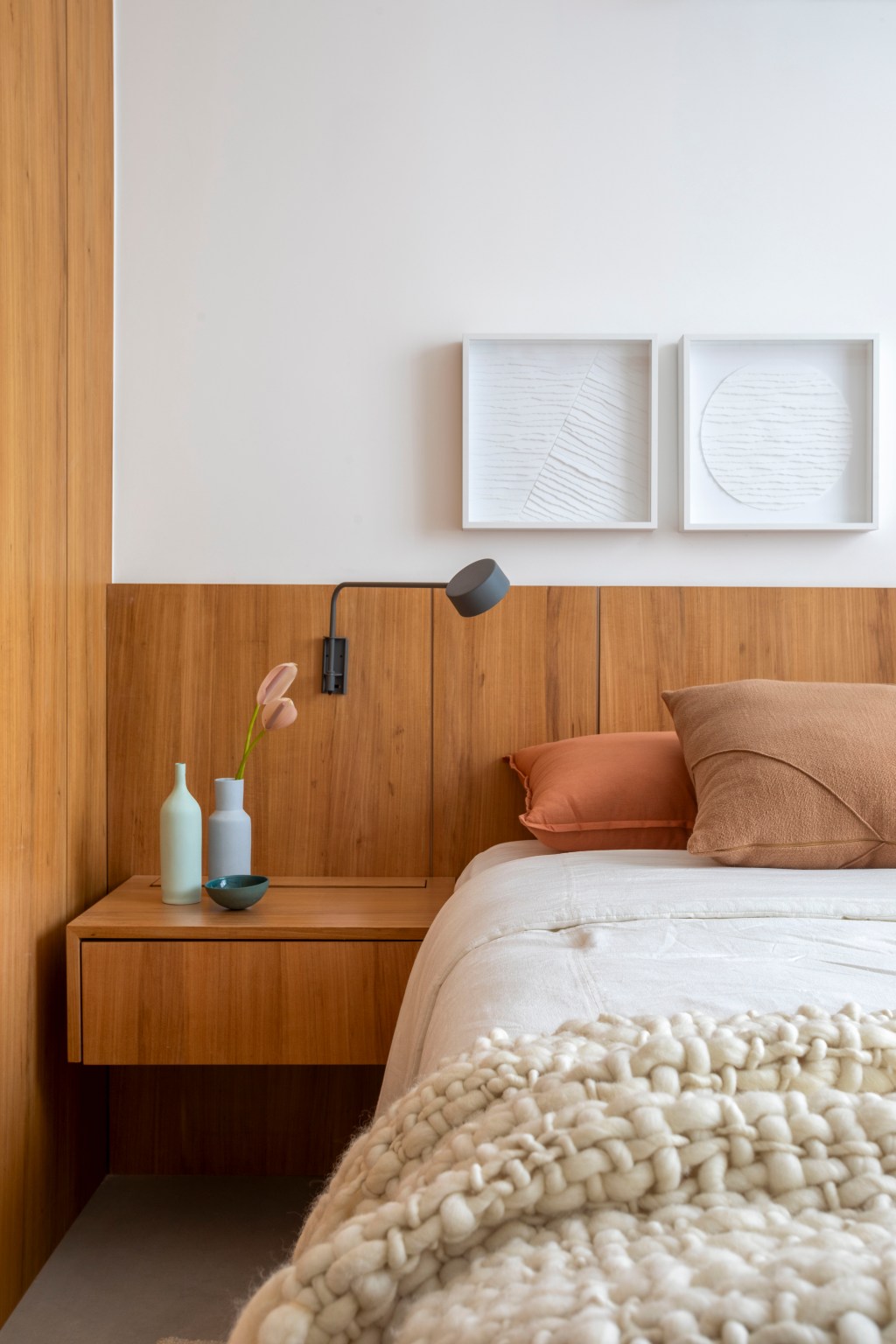 Branco e madeira criam décor cozy em apartamento de 70 m². Projeto de Rafael Ramos. Na foto, quarto de casal com cabeceira de madeira e quadros.